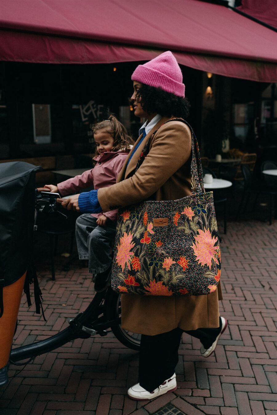 Vrouw heeft de flowa tas uit de collectie van Wood & Cricket over haar schouder en loopt met de bakfiets door de stad